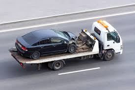 A black car being towed on a flatbed tow truck on a highway.