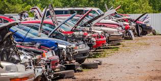 A row of junk cars in a salvage yard with open hoods, showcasing their engines and parts.